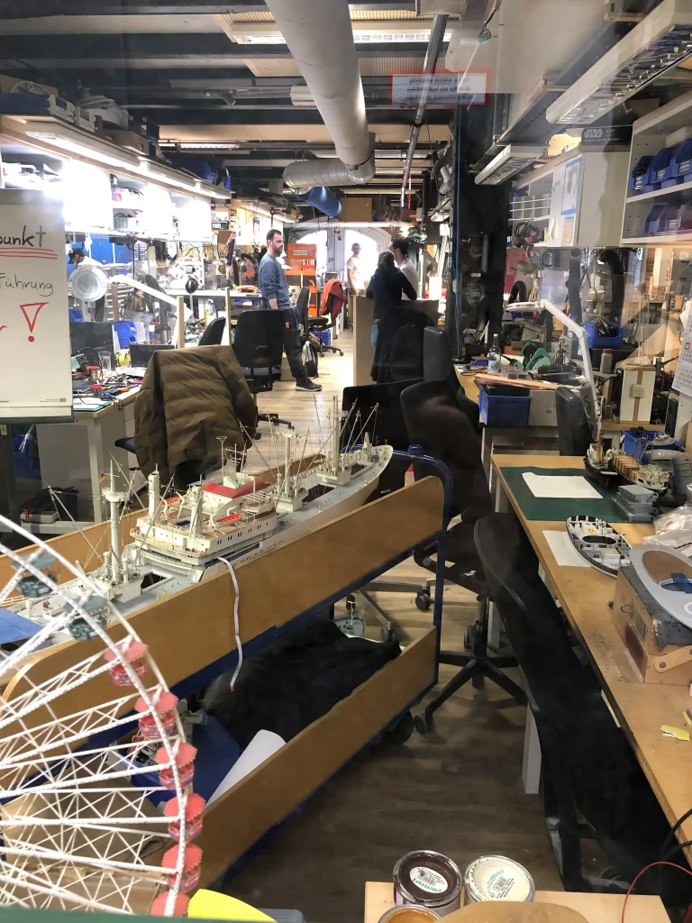Blick in die Werkstatt mit Modellen eines Schiffs und eines Riesenrads, Arbeitsplätzen und Materialien für den Modellbau